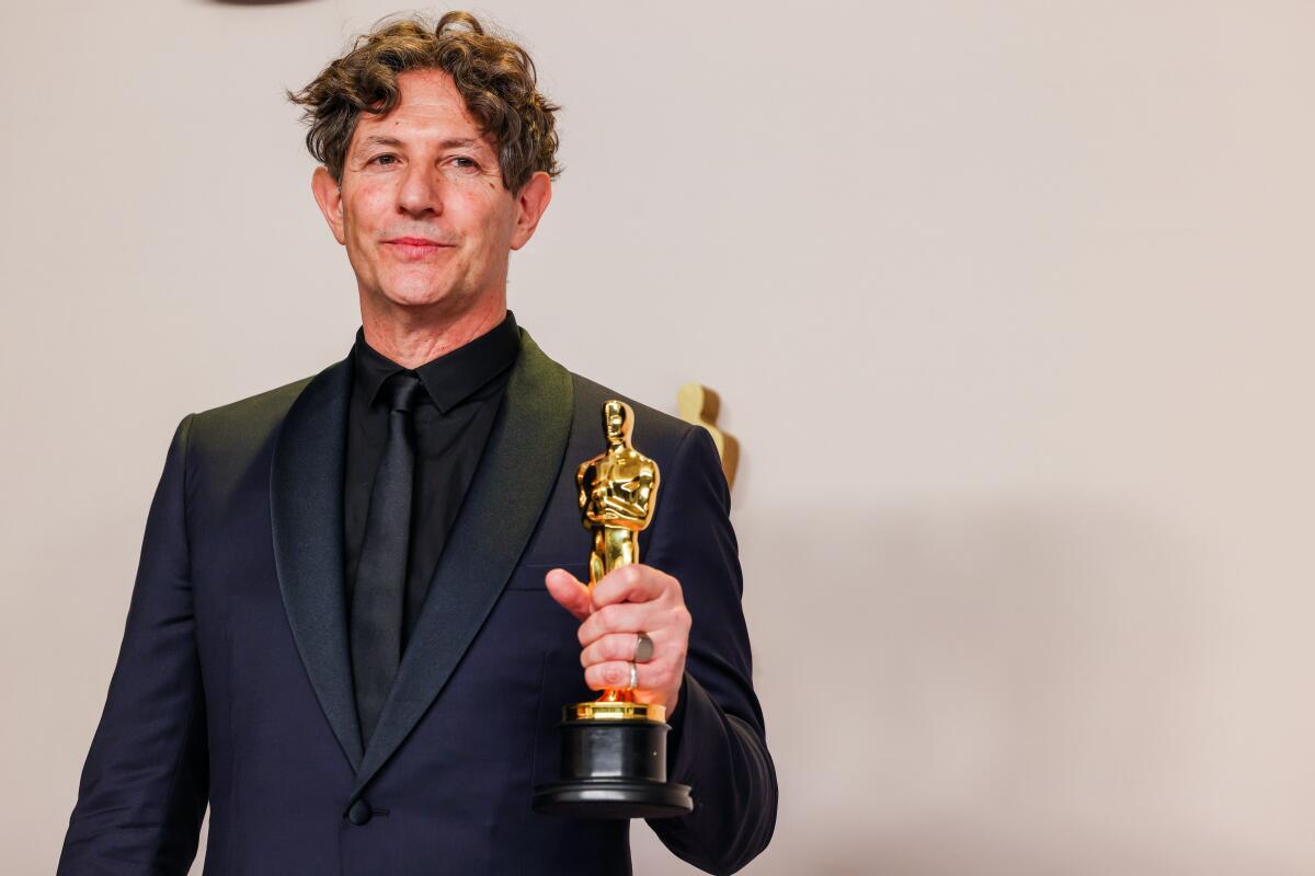 A man in a black tuxedo holds an Oscar.