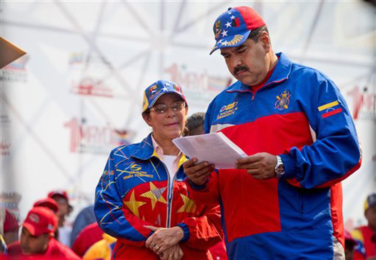 El presidente de Venezuela, Nicol·s Maduro, a la derecha, lee un documento junto a la primera dama, Cilia Flores, a su llegada para una marcha del Primero de Mayo en Caracas, Venezuela, el viernes 1 de mayo de 2015. Maduro dijo en la marcha que elevarÌa el salario mÌnimo y las pensiones para los jubilados en un 30%, llevando el salario mÌnimo a unos 6.700 bolÌvares al mes. Eso son unos 1.000 dÛlares al tipo de cambio oficial del paÌs, pero menos de 25 dÛlares seg¿n la tasa del mercado negro utilizada de forma generalizada para marcar precios. (AP Foto/Fernando Llano)