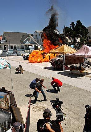 Actors Daniela Ruah, from left, Chris O'Donnell and LL Cool J crouch as a car is blown up on Ocean Front Walk in Venice during shooting of an episode of "NCIS: Los Angeles." The CBS series films extensively on L.A. streets.