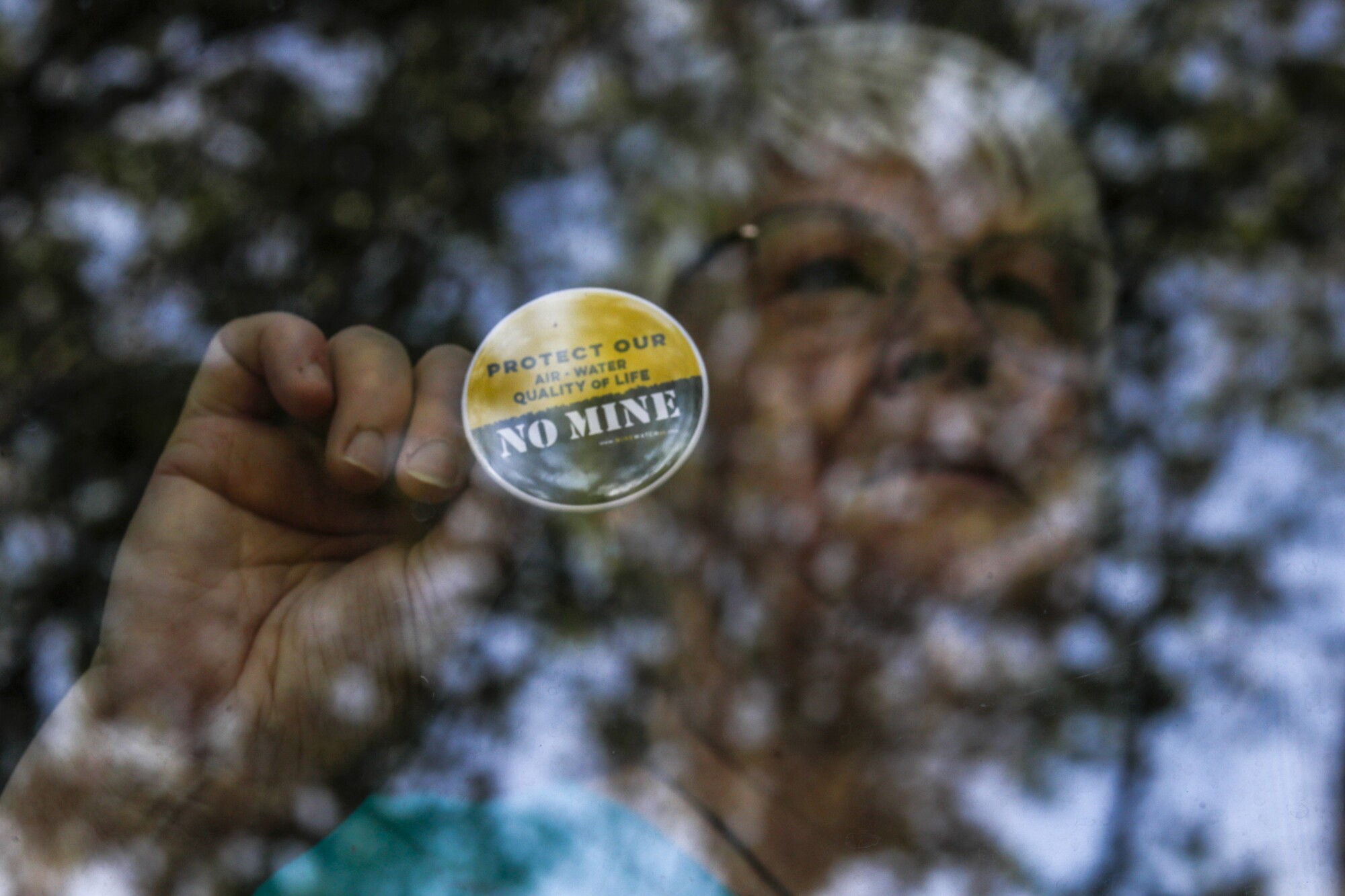 A woman stands in a window displaying a sticker that reads, "No mine"