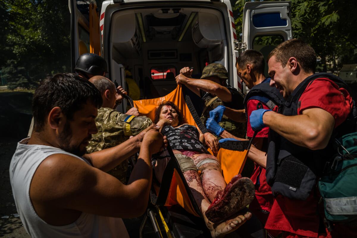  Men, some in fatigues, lift a bloodstained woman lying in a sling into the back of an ambulance 