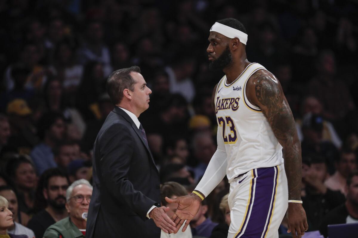 Lakers coach Frank Vogel and forward LeBron James slap hands as the All-Star forward comes off the court during a break in play against the Warriors on Oct. 16, 2019.