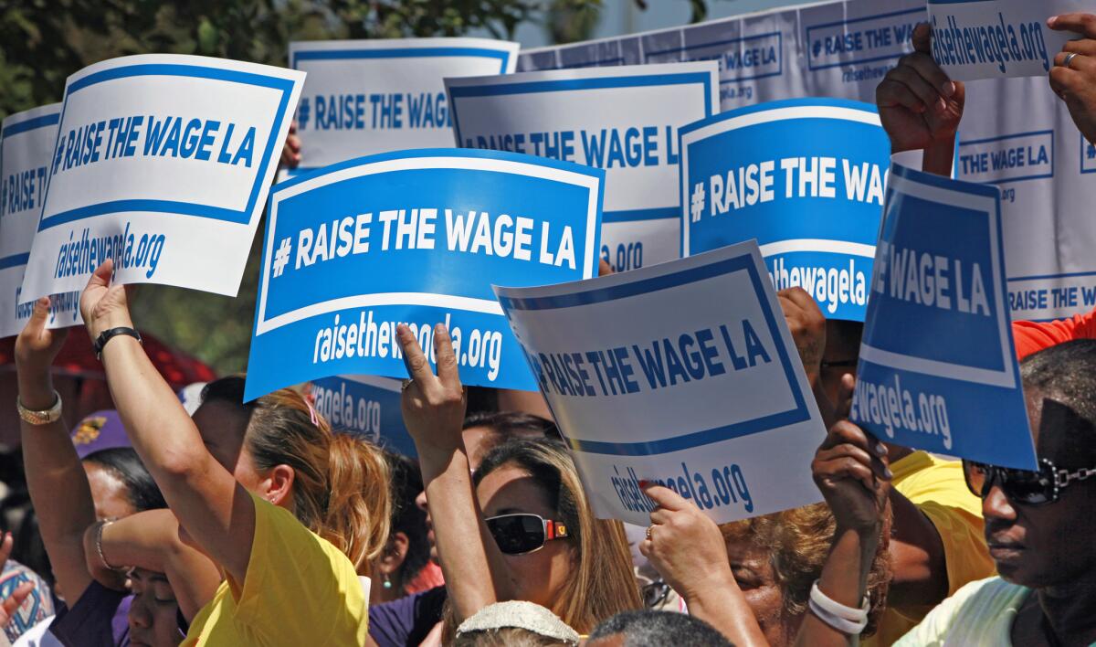 Supporters carry signs to raise the minimum wage in Los Angeles as they listen to Mayor Eric Garcetti during an announcement at Martin Luther King Jr. Park on Thursday.