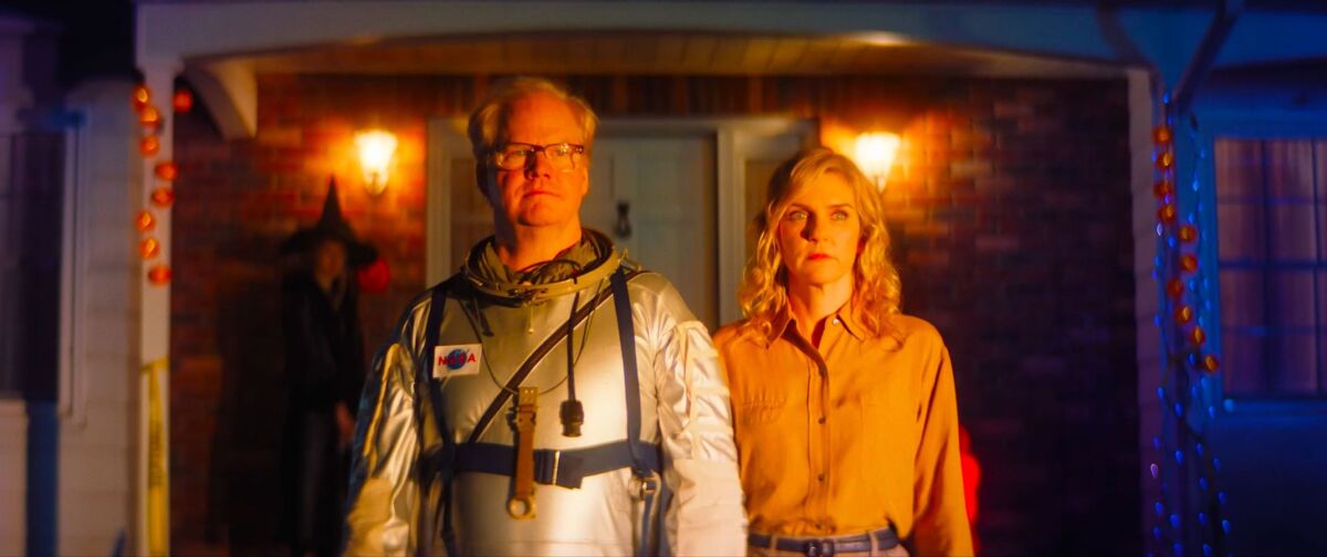 A man in an astronaut suit and a woman stand in front of a house in the movie "Linoleum."