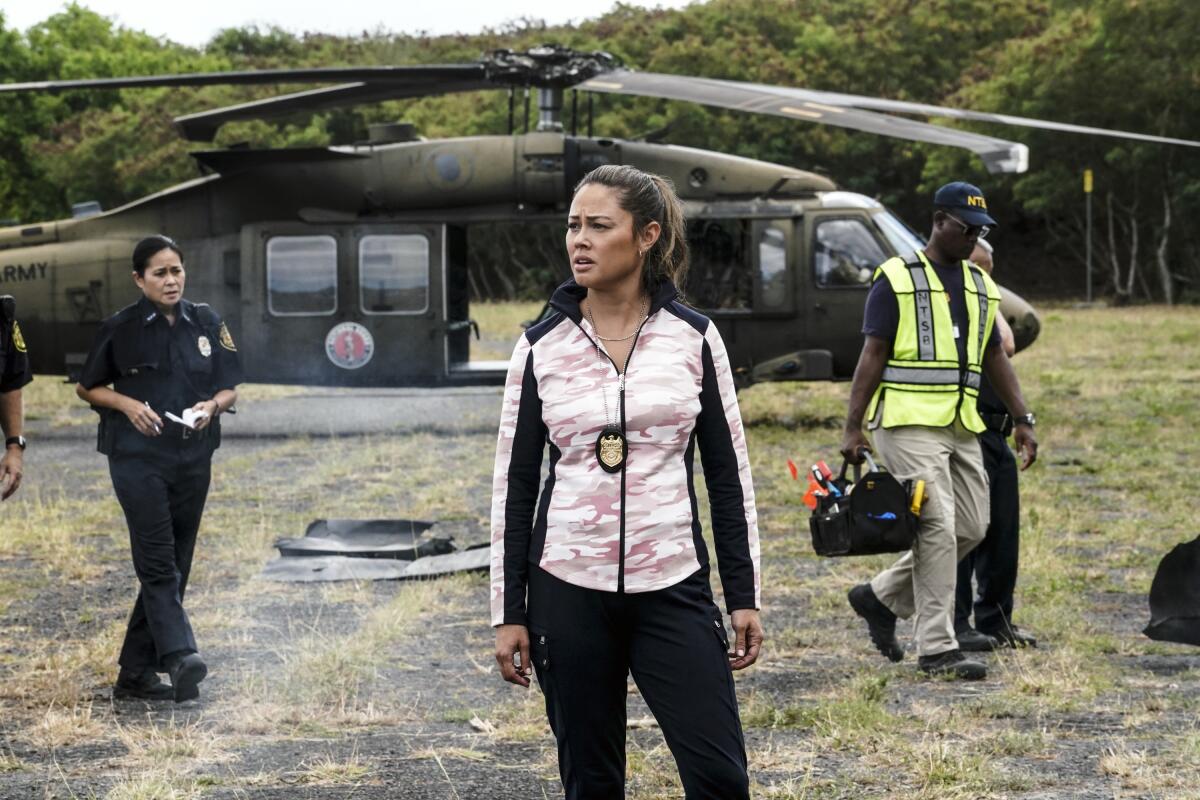 A woman stands with others in front of a helicopter at an "NCIS: Hawai'i" crime scene