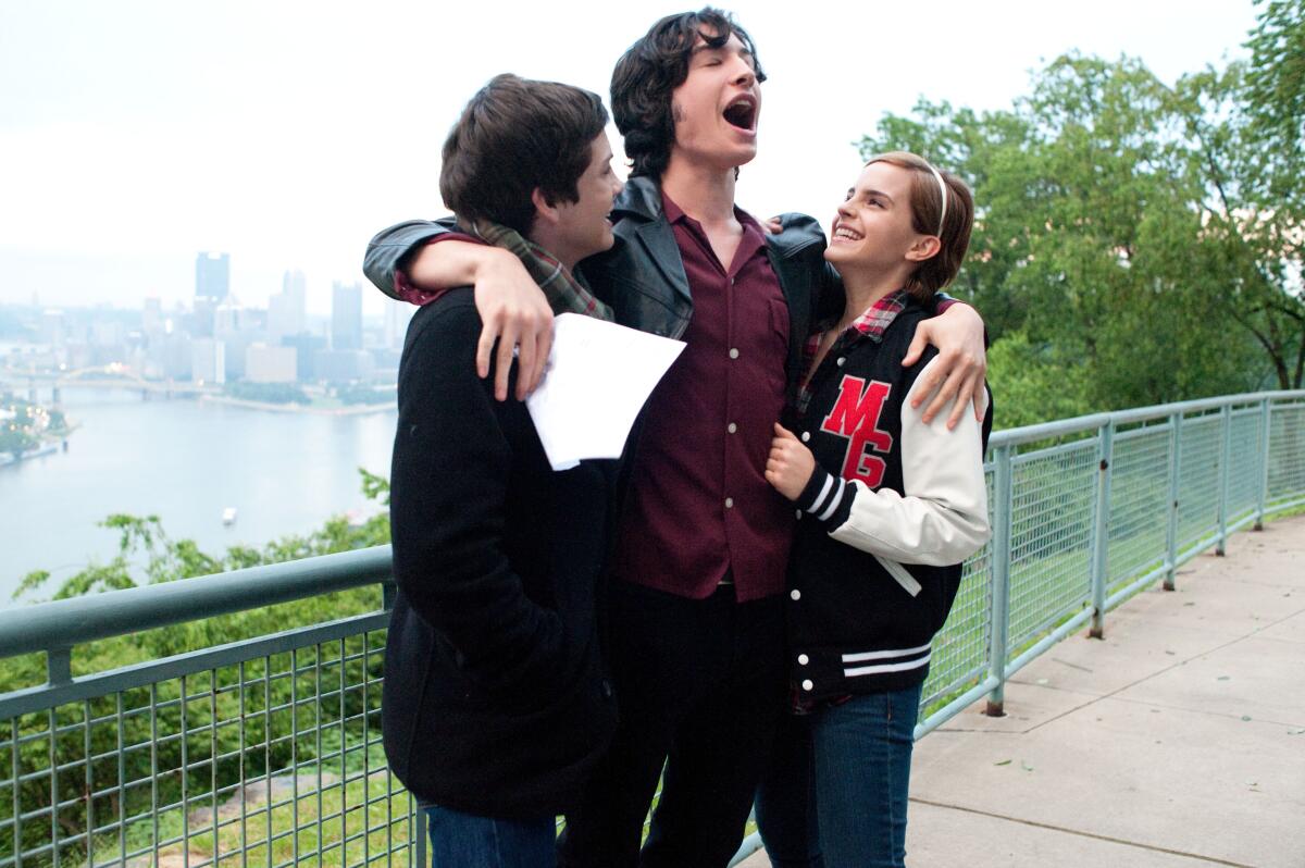 A tall person sings with their arms around a boy and a girl standing on either side of them