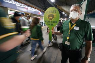 John Abercrombie, an usher for the Oakland Athletics, holds up a sign advising people to wear masks, prior to a baseball game between the Ahletics and the Houston Astros on Friday, April 2, 2021, in Oakland, Calif. (AP Photo/Tony Avelar)