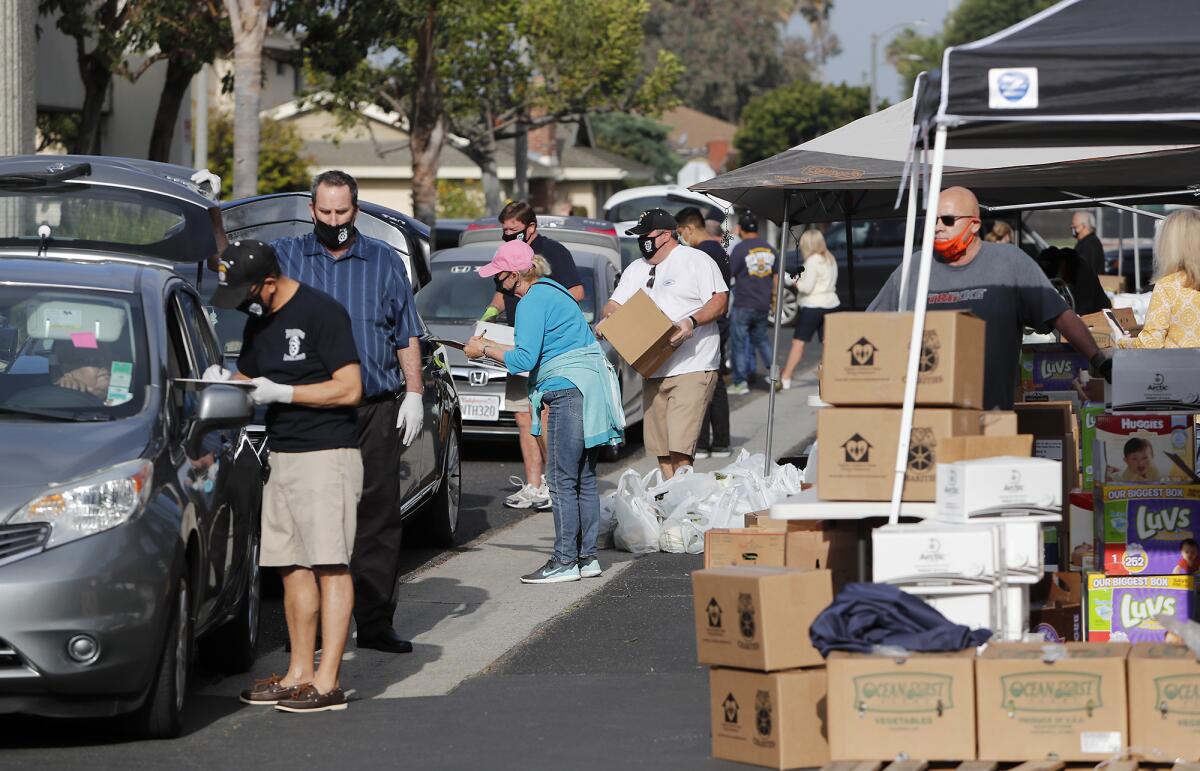 Volunteers take note of names, phone numbers and family size as others load food at Colette's Children's Home on Saturday morning in Huntington Beach.