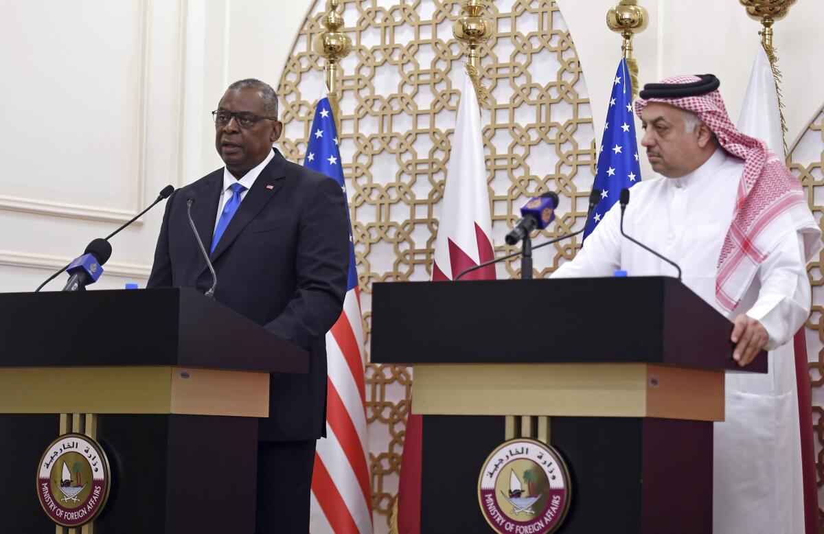 Two men, one in business suit and the other in robes and keffiyeh, stand at lecterns in an outdoor news conference