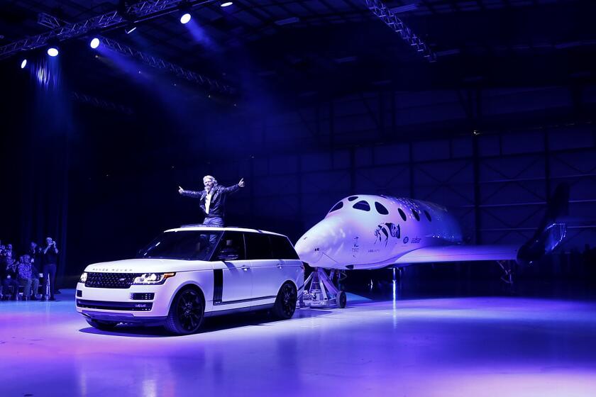 Richard Branson stands in an SUV as it tows the new Virgin Galactic SpaceShipTwo, named VSS Unity, at an unveiling event at the Mojave Air and Space Port Friday. The new vehicle replaces the company's previous SpaceShipTwo, which broke apart in midair nearly 16 months ago, killing one of two pilots.