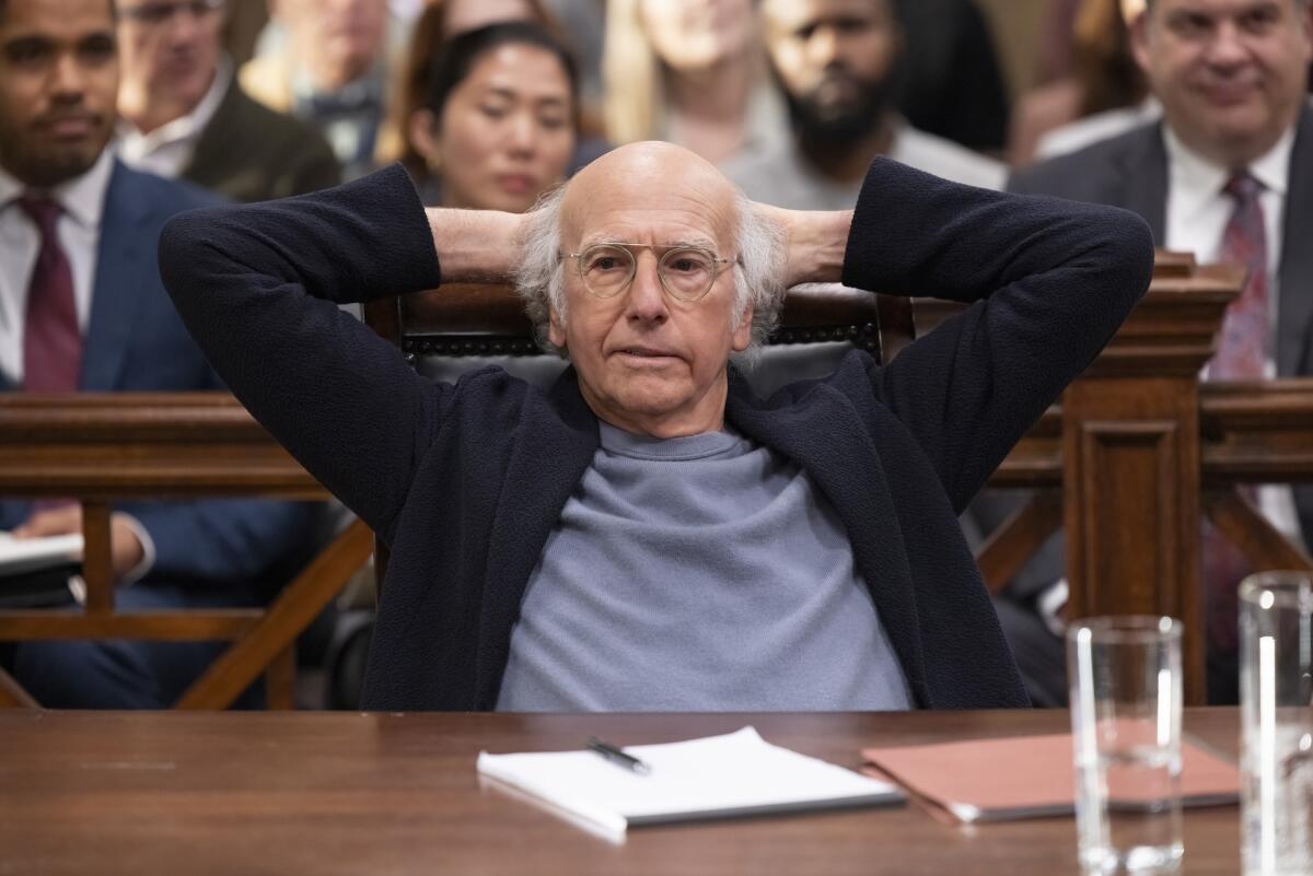 A man sitting in a courtroom with his hands resting on the back of his head.