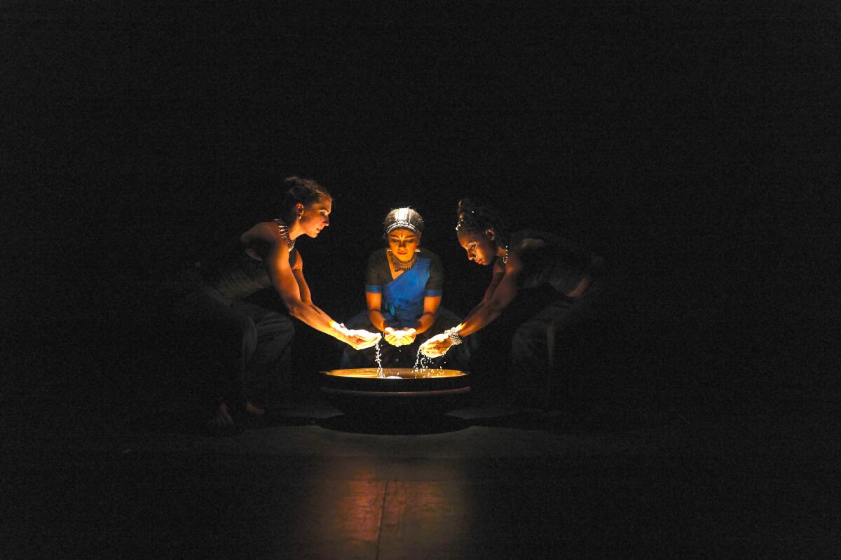 three women lift water with their hands from a large bowl