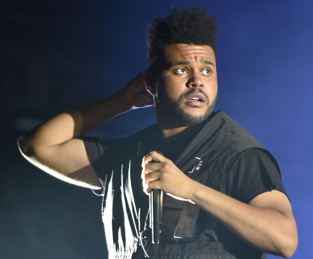 The Weeknd holds a microphone on stage.