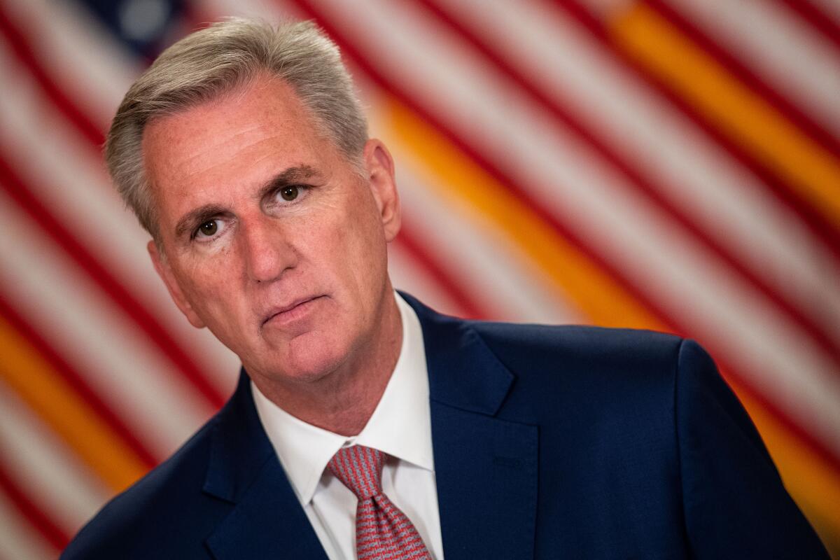 A slanted photo of Speaker Kevin McCarthy from the shoulders up, against a background resembling a modified American flag