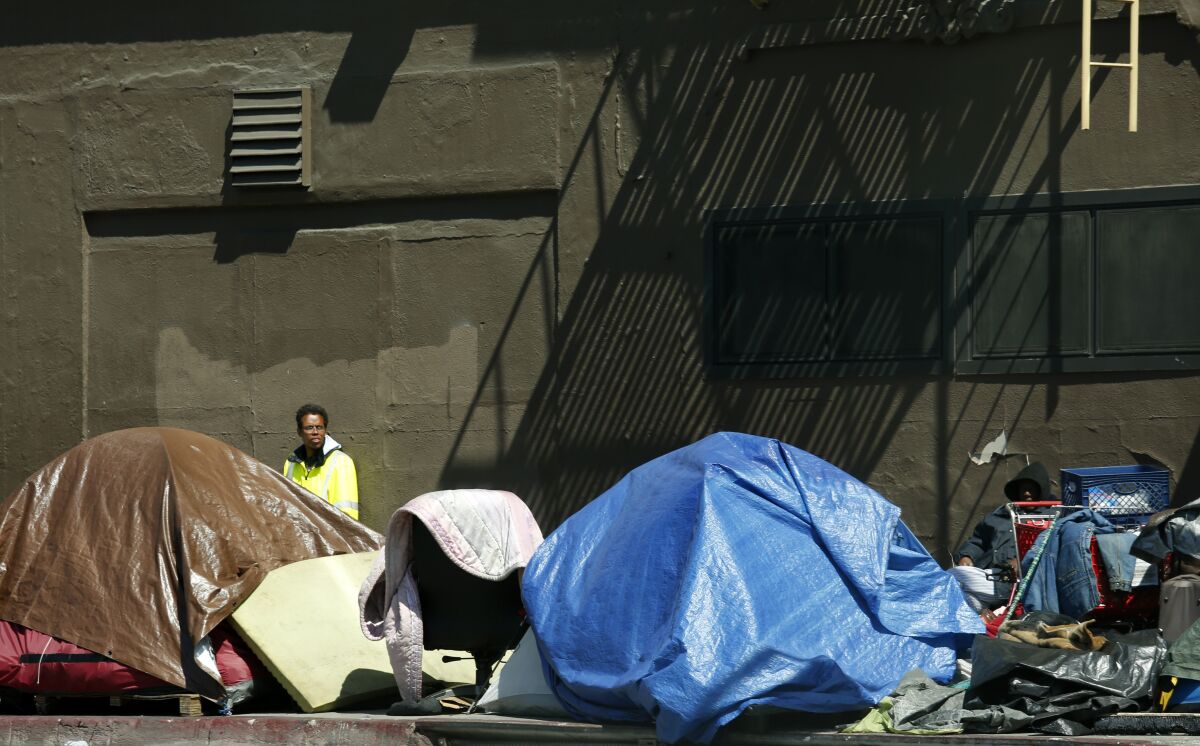 A man stands behind a cluster of tents in downtown Los Angeles.
