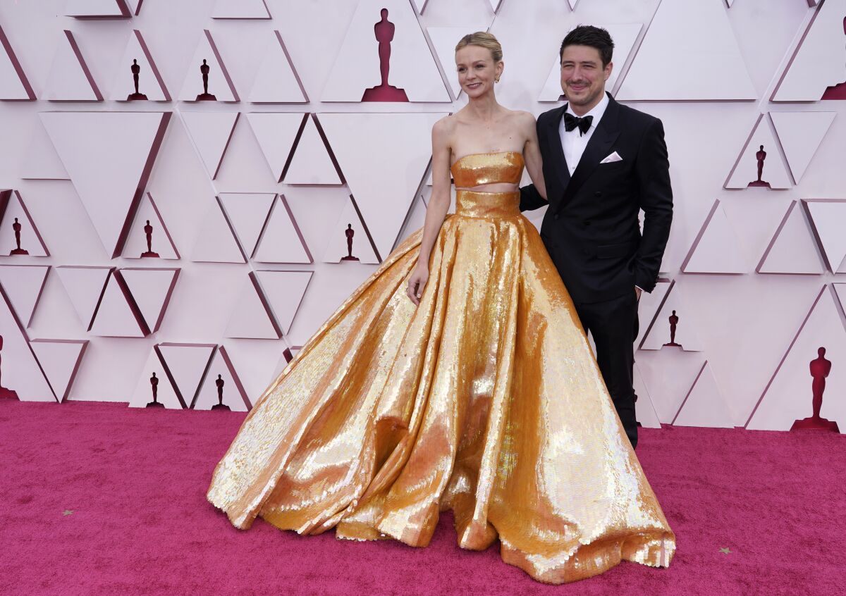 A woman in a gold ballgown and a man in a tuxedo walk the red carpet at an awards show.
