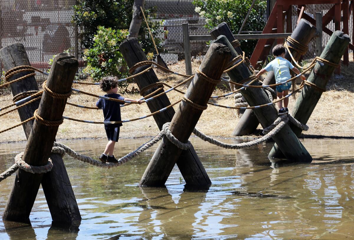 Kids traverse a lagoon via a rope bridge at Huntington Beach's Adventure Playground in Central Park Saturday. 