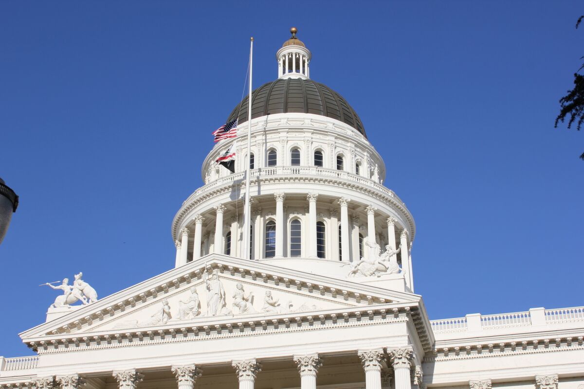 Flags fly at half-staff in front of the white dome of the California state Capitol building on a sunny day