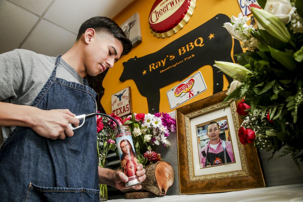 A young man lights a prayer candle for his father. On the table is a framed photo of Rene "Ray" Ramirez, and flowers.