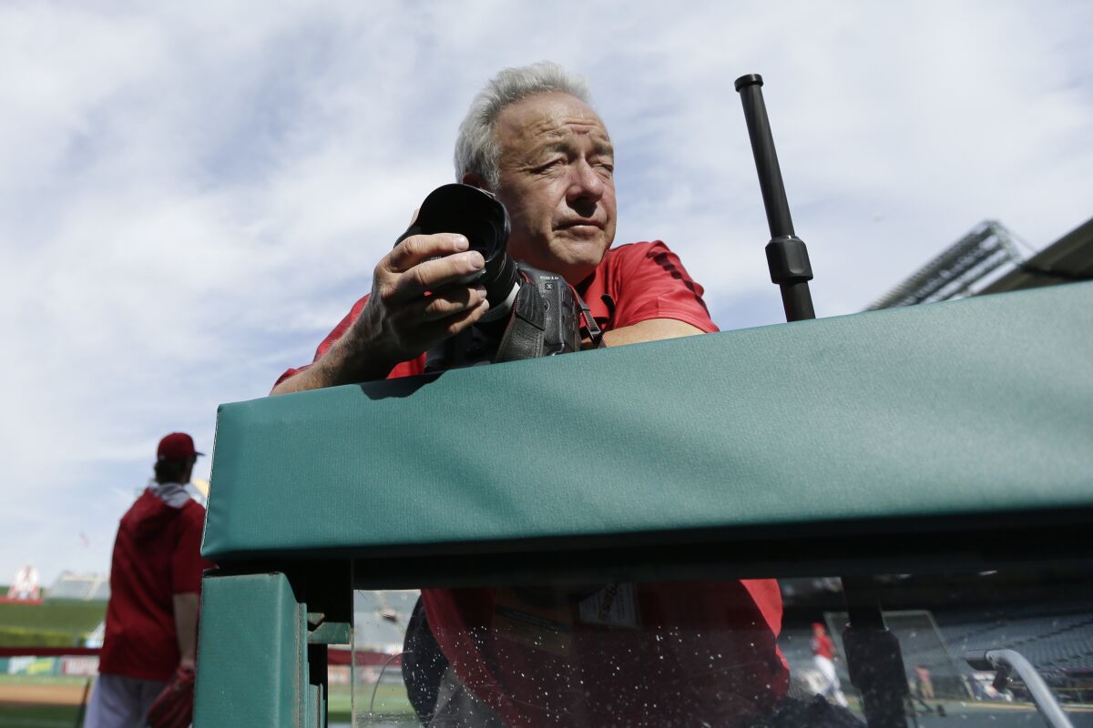 FILE - Photographer Lenny Ignelzi leans against a dugout rail Oct. 3, 2014, before Game 2 of baseball's AL Division Series between the Los Angeles Angels of Anaheim and the Kansas City Royals in Anaheim, Calif. Ignelzi, whose knack for being in the right place at the right time produced breathtaking images of Hall of Fame sports figures, devastating wildfires and other major news over 37 years as photographer for The Associated Press in San Diego, has died. He was 74. Ignelzi died Friday, April 29, 2022, in Las Vegas of cerebral amyloid angiopathy, a brain condition that triggers frequent strokes, according to his wife, Bobbi. (AP Photo/Gregory Bull, File)