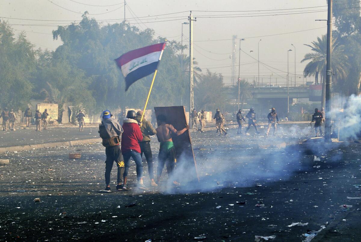 Protesters wave the national flag as security forces fire tear gas during an ongoing protest in Baghdad.