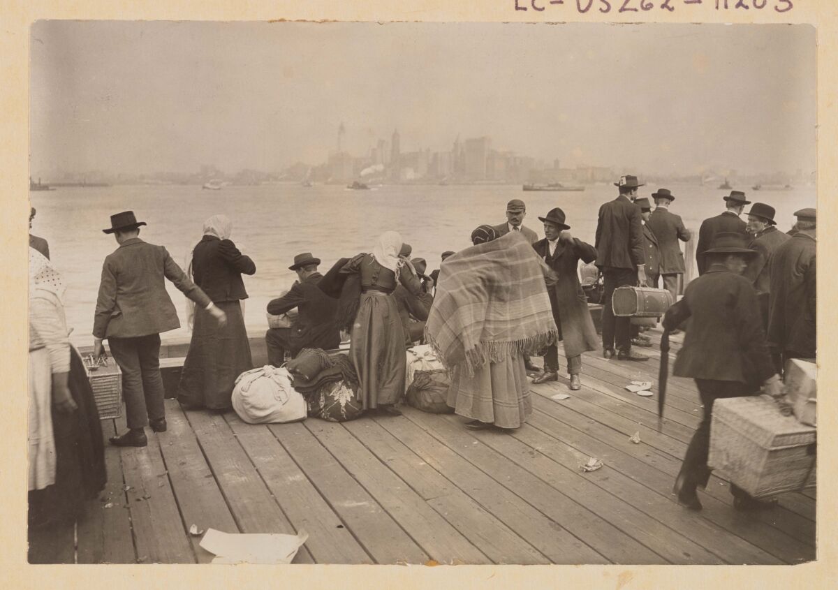 Zwart-witfoto van immigranten op een stoep met uitzicht op de skyline van New York City