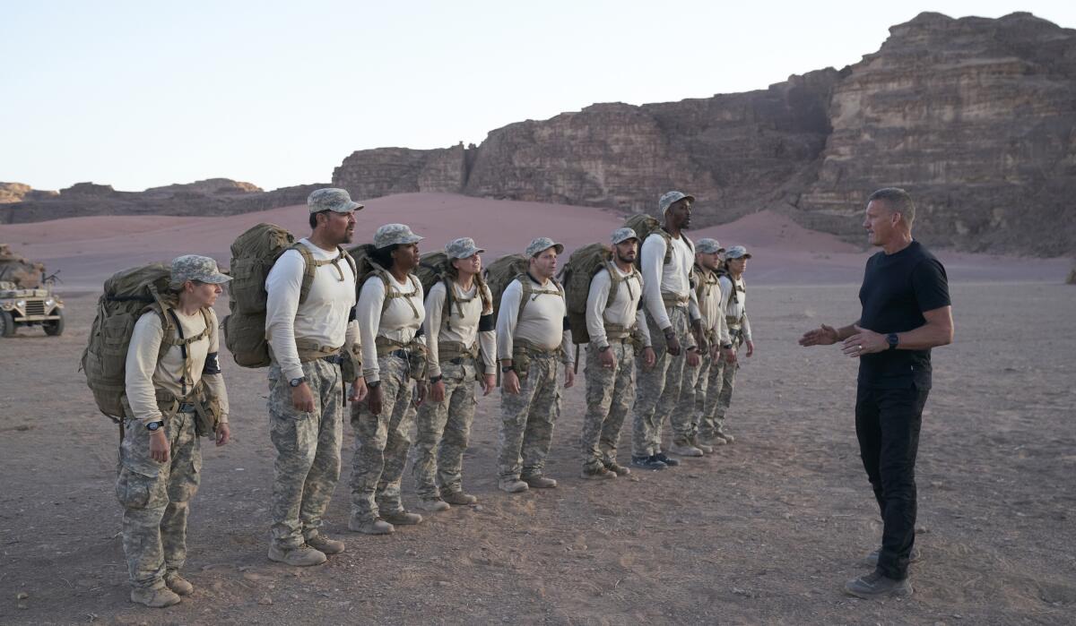 Celebrities line up with large backpacks in a desert