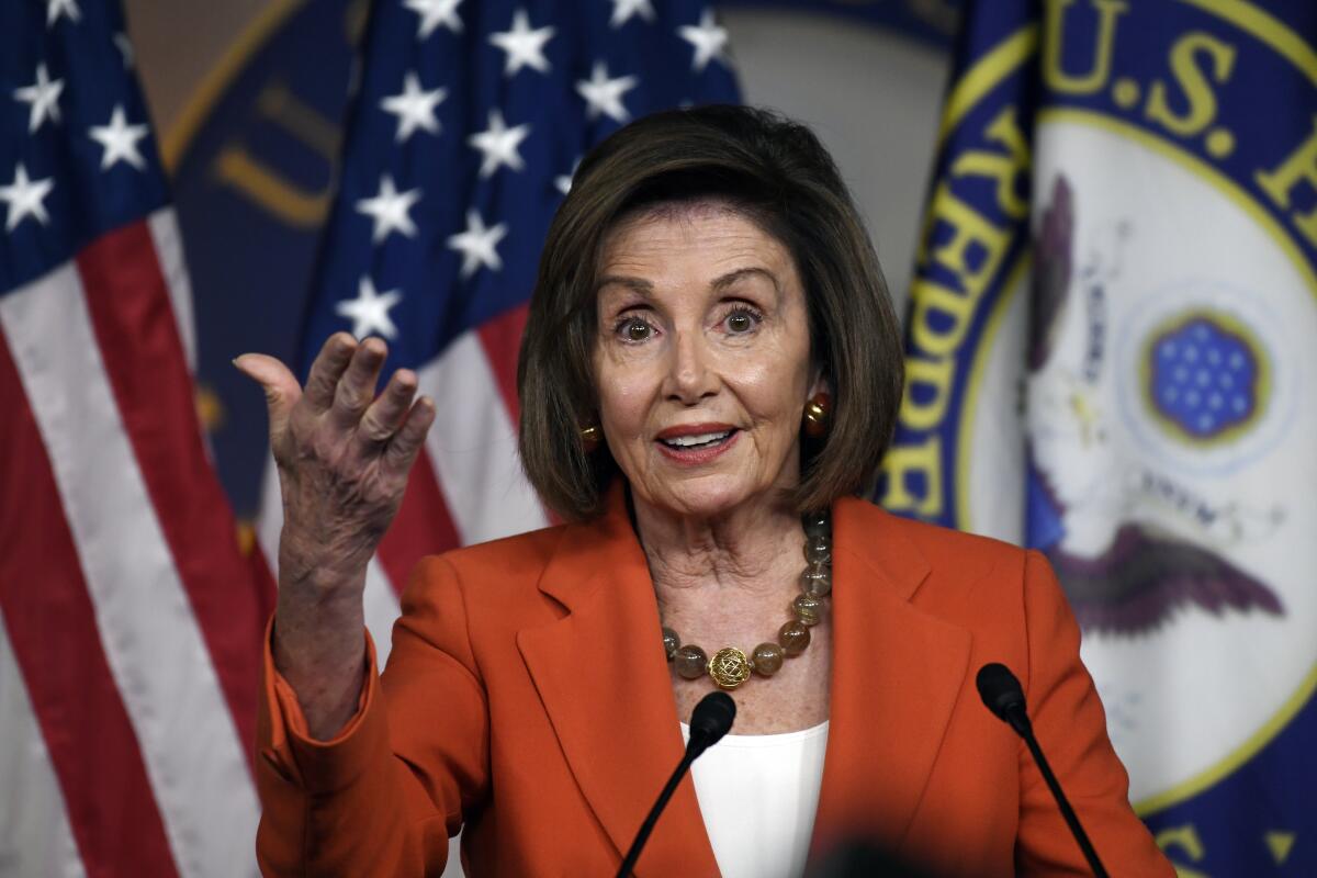 A woman in an orange pantsuit speaks in front of a microphone while addressing a crowd.