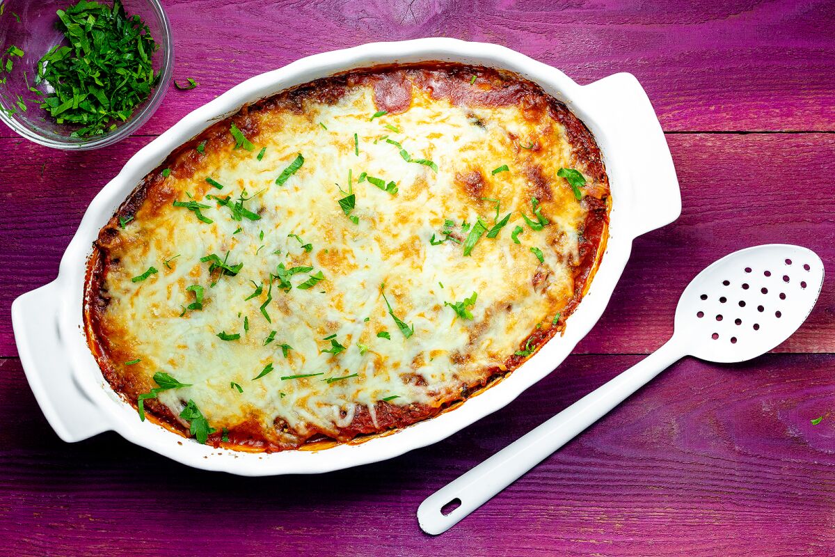 A spaghetti squash casserole in an oval baking dish, topped with melted cheese and garnished with chopped parsley.
