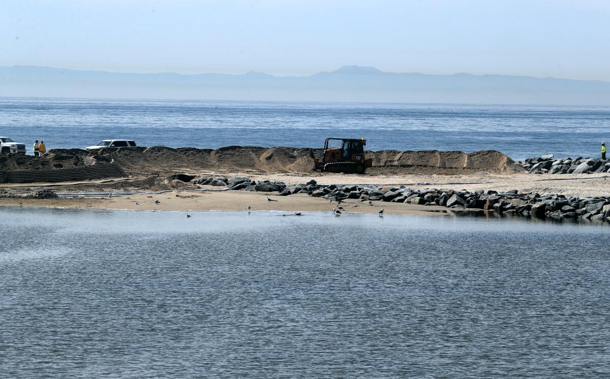 A bulldozer creates a berm at the mouth of the Santa Ana river in Newport Beach on Sunday.