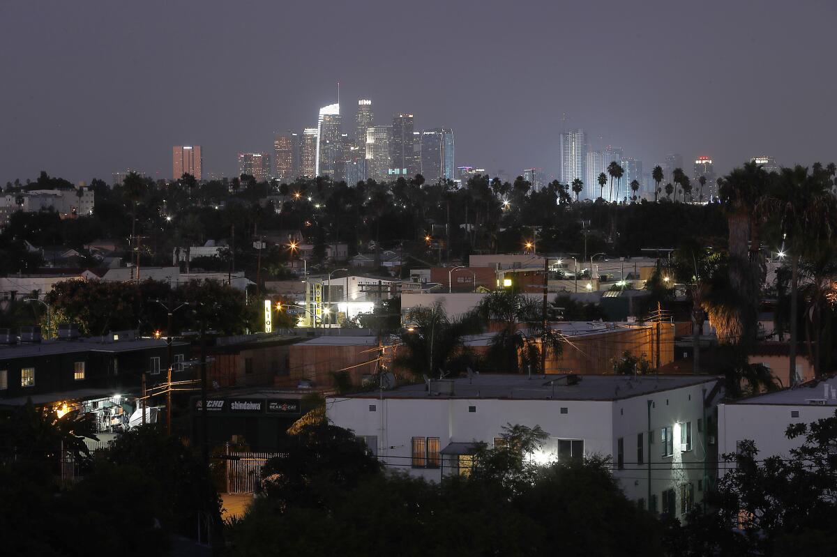 Dusk descends on the residential streets of the Crenshaw District in South L.A. with the downtown Los Angeles skyline in the background.
