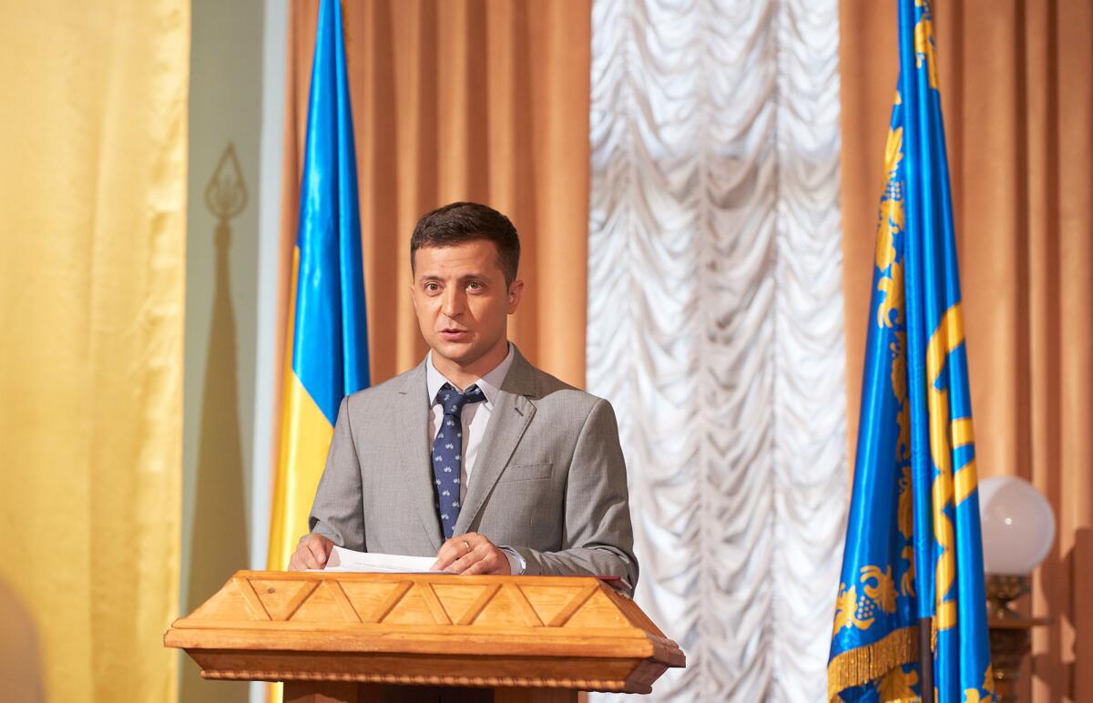 A man stands at a podium with blue and yellow Ukrainian flags behind him.