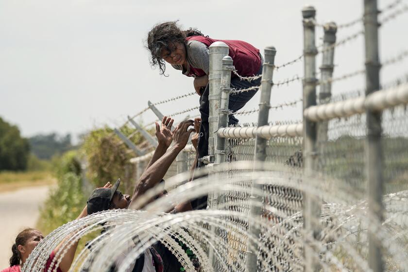 Migrants who crossed the Rio Grande from Mexico into the U.S. climb a fence with barbed wire and concertina wire, Monday, Aug. 21, 2023, in Eagle Pass, Texas. (AP Photo/Eric Gay)