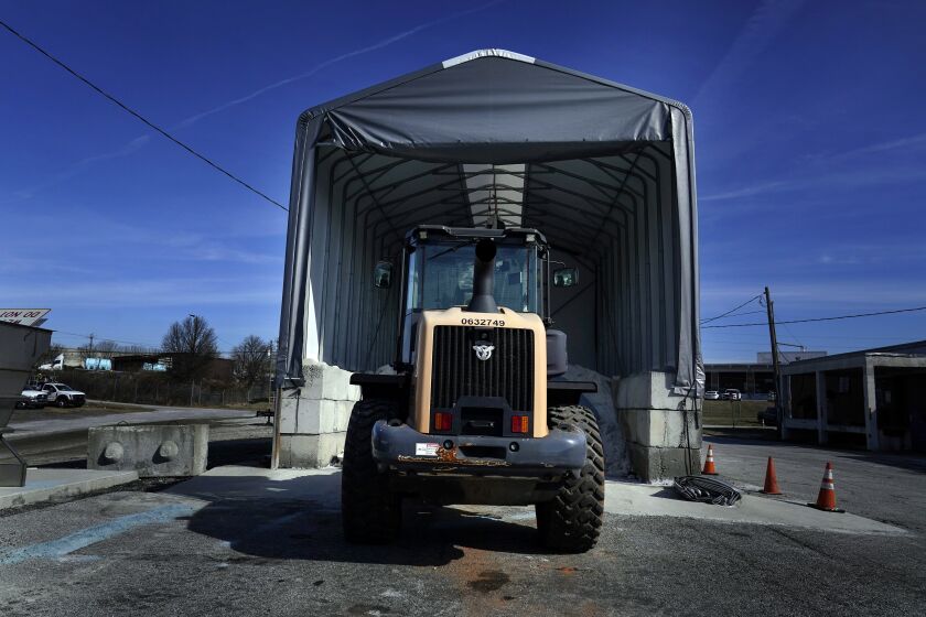 A tractor sits in front of a pile of salt used to create a brine that will help clear road of ice and snow ahead of a winter storm at the GDOT's Maintenance Activities Unit location on Friday, Jan. 14, 2022, in Forest Park, Ga. A winter storm is headed south that could effect much of Georgia through Sunday. (AP Photo/Brynn Anderson)