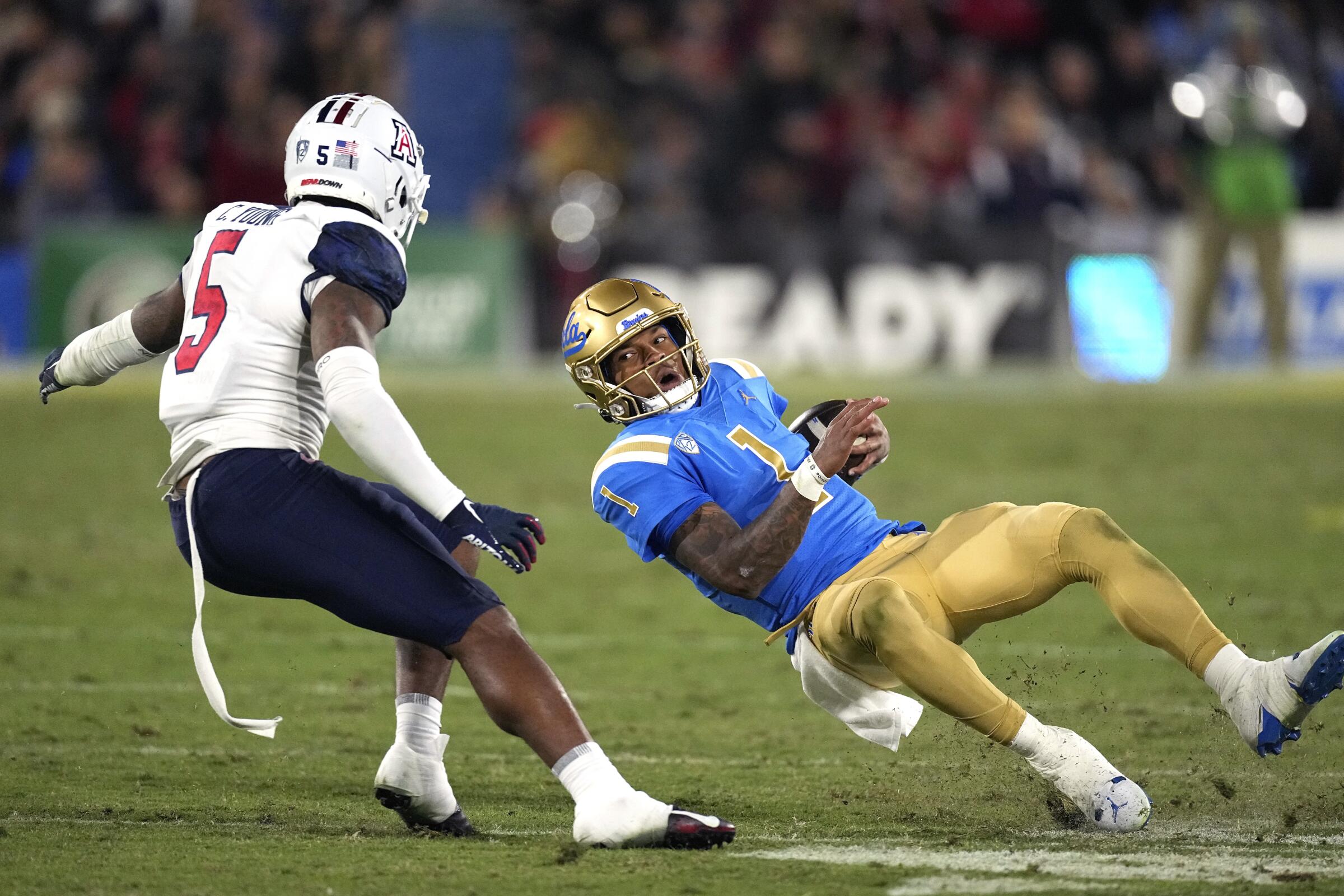 UCLA quarterback Dorian Thompson-Robinson, right, slips while under pressure from Arizona safety Christian Young.