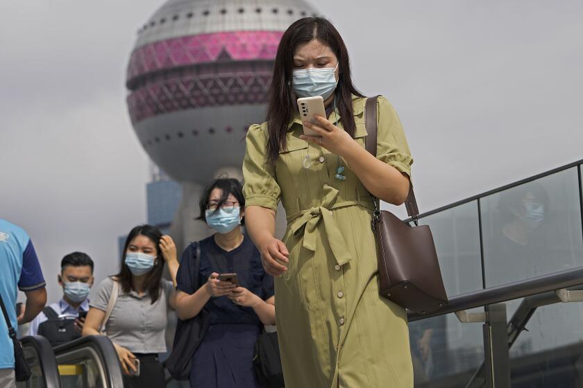 People wearing face masks to help protect from coronavirus using their smartphones walk on a pedestrian overhead bridge in front of the Oriental Pearl TV Tower at the Pudong Financial District in Shanghai, China, on Aug. 25, 2021. Chinese regulators will exercise greater control over the algorithms used by Chinese technology firms to personalize and recommend content, in the latest move in a regulation spree across the internet sector. (AP Photo/Andy Wong)
