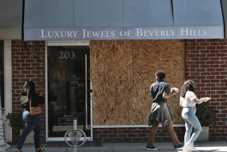 Pedestrians walk past a boarded up Luxury Jewels of Beverly Hills on Wednesday, March 23, 2022 in Beverly Hills, Calif. Los Angeles police are warning people that wearing expensive jewelry in public could make them a target for thieves — a note of caution as robberies are up citywide. The police department's suggestion Tuesday, March 22, came as robbers smashed the front window of a Beverly Hills jewelry store in broad daylight and fled with millions of dollars' worth of merchandise. (AP Photo/Richard Vogel)