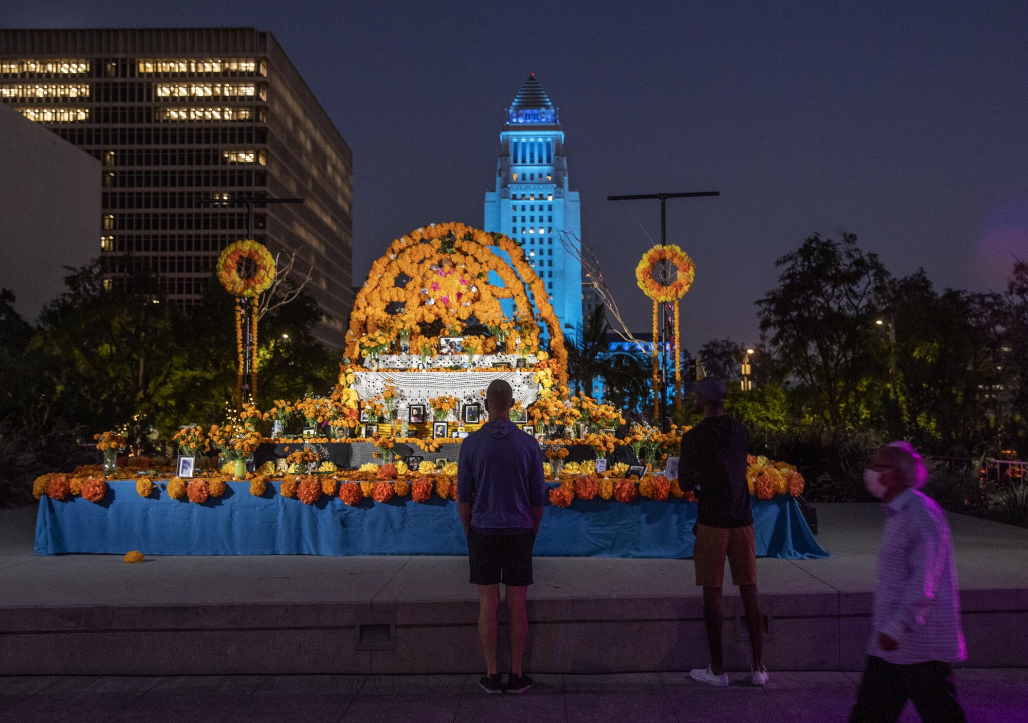 A community Dia de los Muertos altar in Grand Park, with City Hall, lit in blue, behind it.