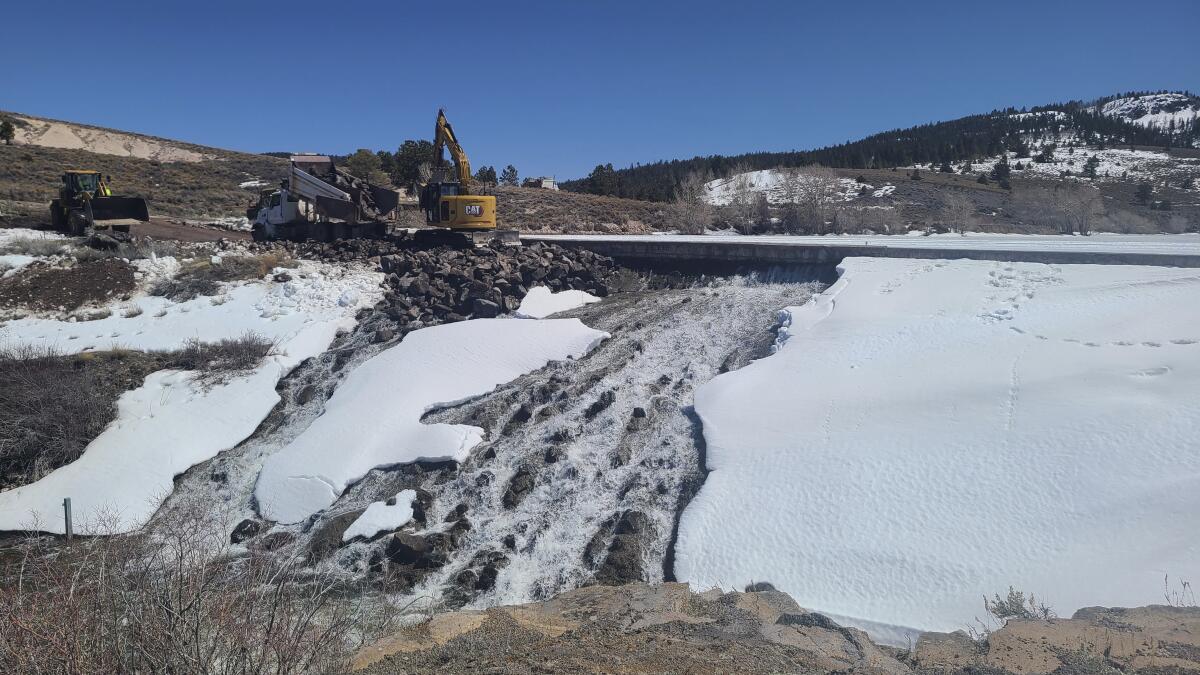 Crews use machinery to bolster a dam.
