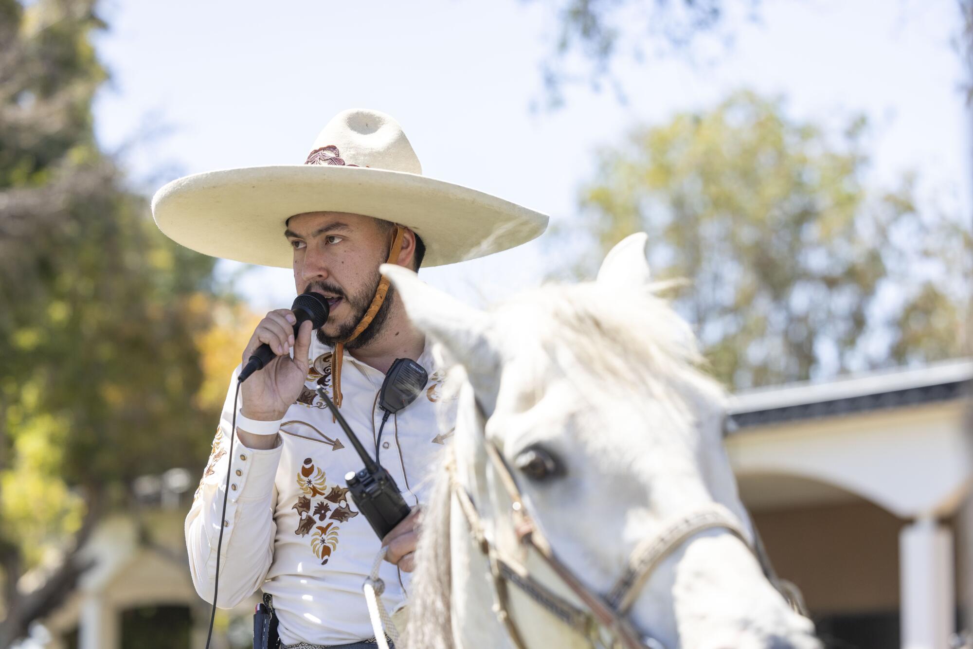 A man in a sombrero who is riding a horse speaks into a microphone