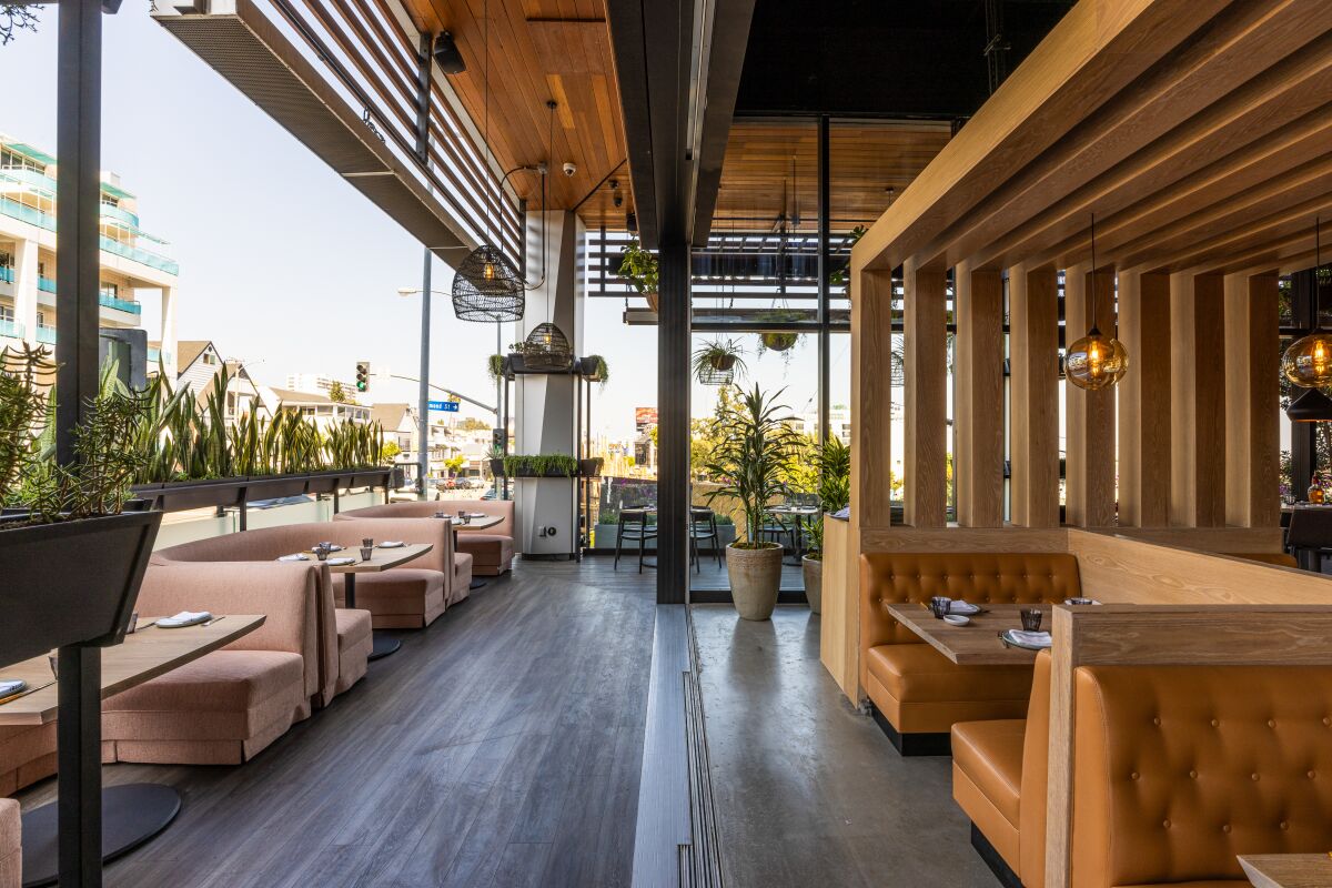 The indoor-outdoor dining room of Charcoal Sunset. Pink booths sit streetside to the left, with wooden booths inside at right