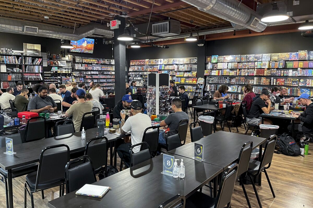 People sitting at long tables playing games, surrounded by rentable games on the wall, at Next-Gen Games.