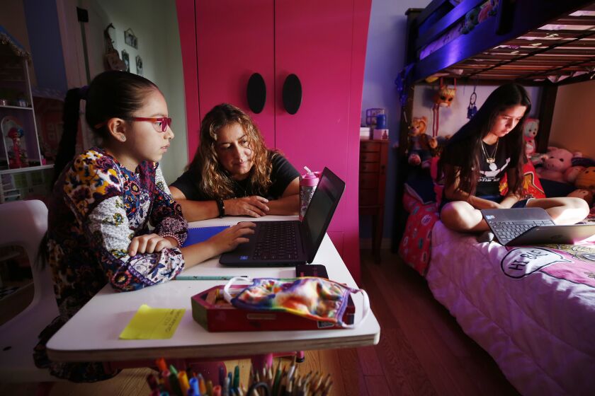 LOS ANGELES, CA - SEPTEMBER 17: 9-year-old Priscilla Guerrero uses a laptop computer for her 4th grade Los Angeles Unified School District online class in her room as mom Sofia Quezada assists her and 13-year-old sister Paulette Guerrero during remote learning lessons at home on September 17, 2020. Boyle Heights on Thursday, Sept. 17, 2020 in Los Angeles, CA. (Al Seib / Los Angeles Times