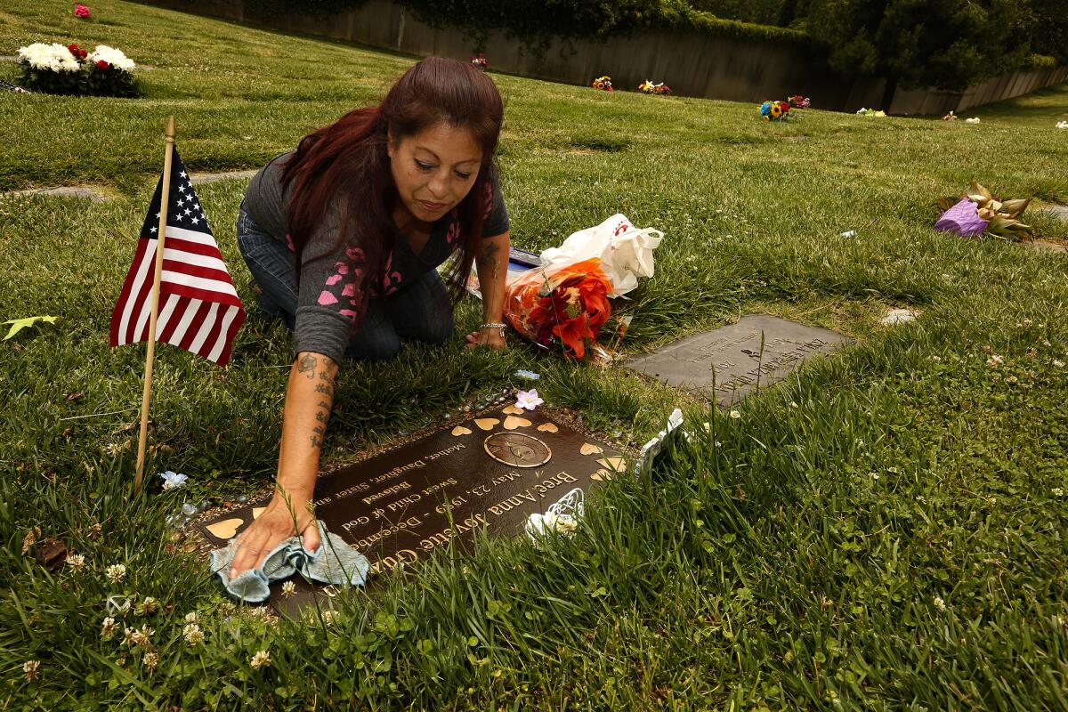 A woman wipes down a grave marker in a cemetery. 