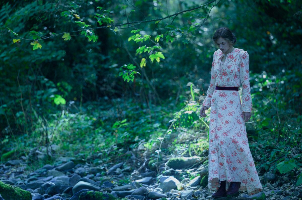 Emma Corrin stands near a stream in a pink and white floral gown in "Lady Chatterley's Lover."