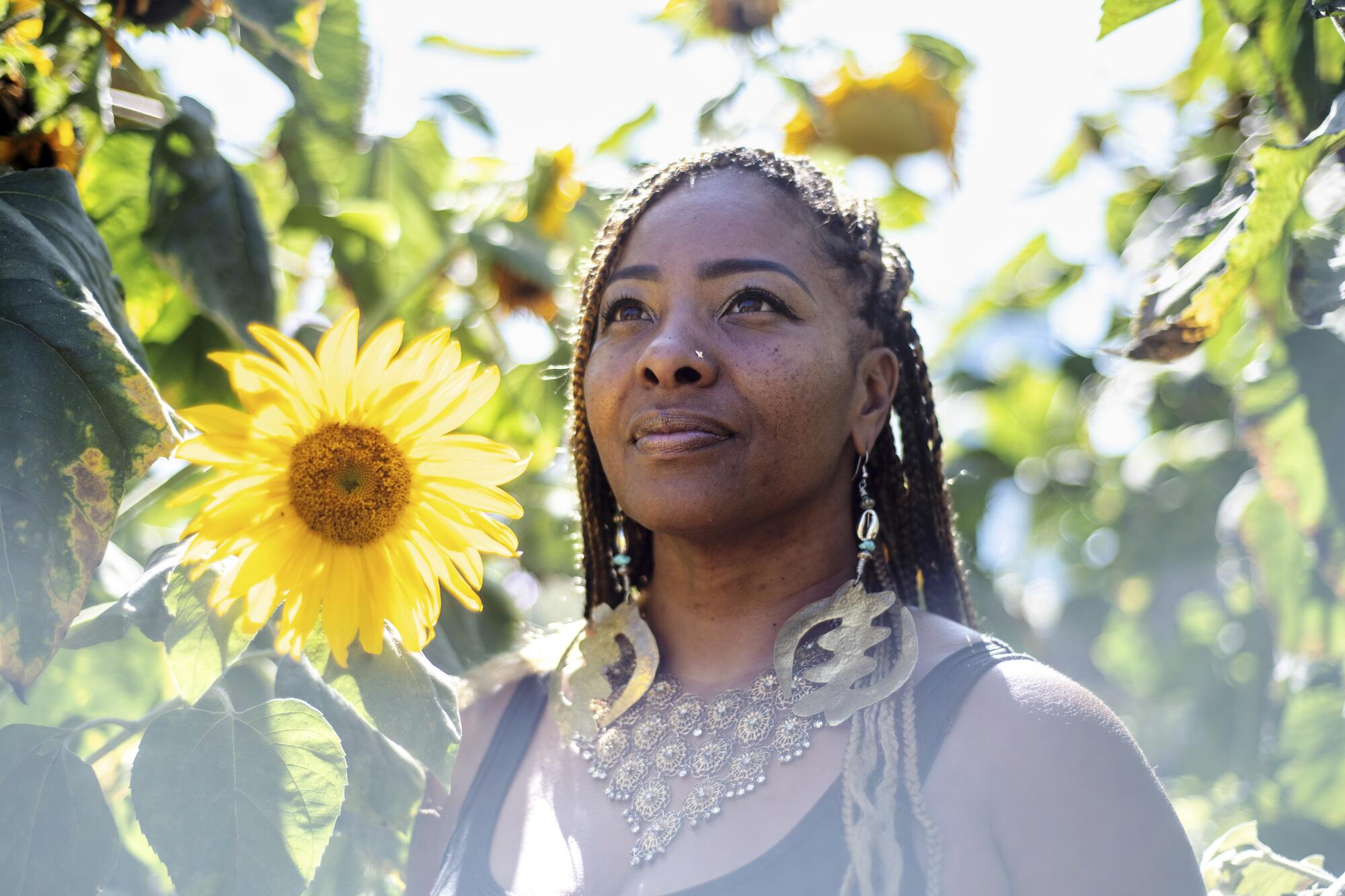 Genea Richardson stands amid sunflowers, looking upward.