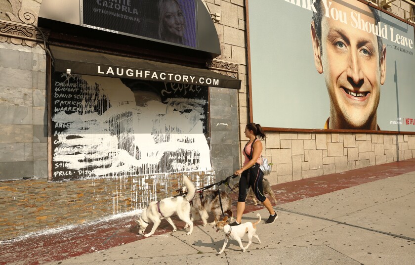 A woman with three dogs on leashes looks at a sign smeared with paint.