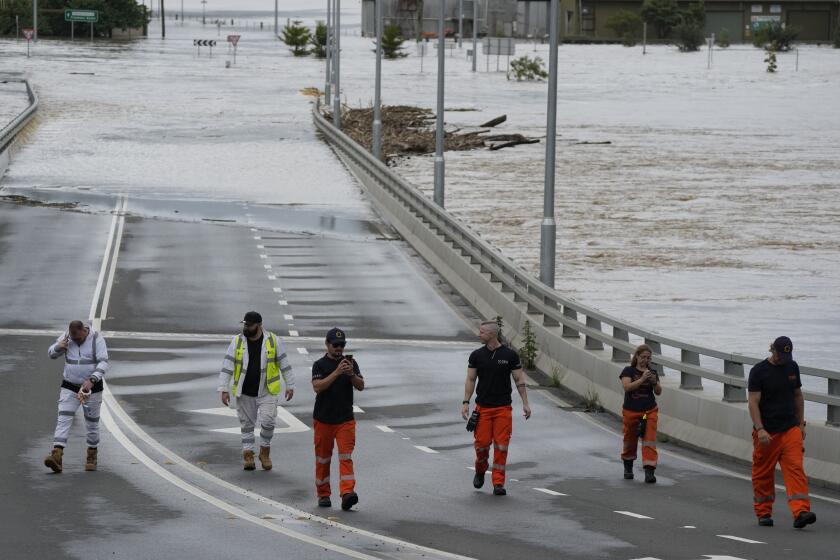 State emergency staff stand near the entrance to the flooded Windsor bridge on the outskirts of Sydney, Australia, Thursday, March 3, 2022. Around 500,000 people in Sydney and its surrounds have been told to evacuate or prepare to flee floodwaters as torrential rain lashes an extraordinarily long stretch of the Australian east coast. (AP Photo/Rick Rycroft)