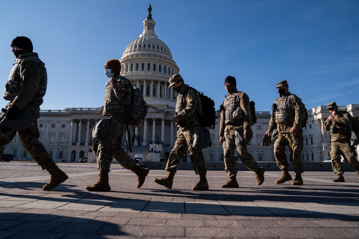 National Guard troops in camouflage fatigues walk in a line in front of the Capitol dome