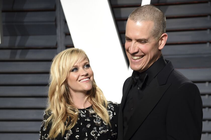 Reese Witherspoon in a black dress looking to a man on her right wearing a black suit